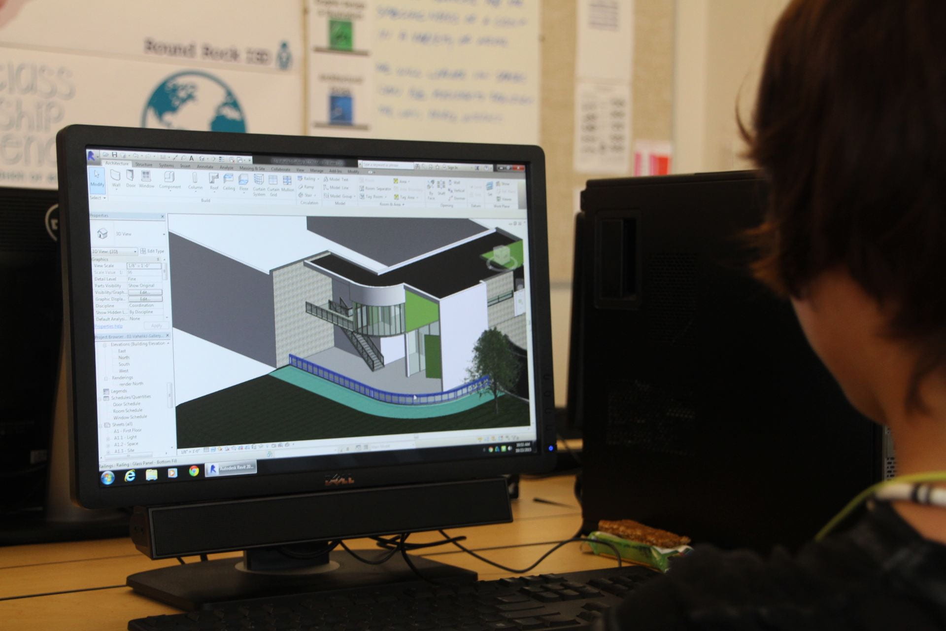 Student viewing computer screen showing 3D design of building