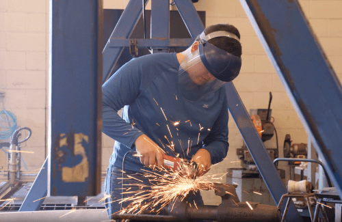 Student using tool to clean metal - sparks are coming from point of contact